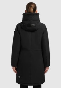 Sort parka med en høj krave med blødt for, sidelommer og en logo detalje nær kanten. Glat stof med mat finish.