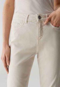 Lichtbeige denim jeans met een getailleerd ontwerp, voorzien van voorzakken en een metalen knoopsluiting. Getextureerde stof met subtiele stikseldetails.