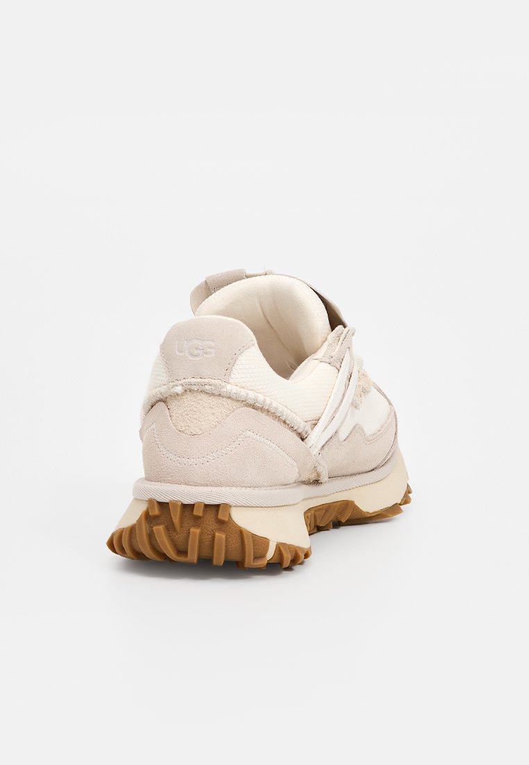 Baskets UGG en suède beige et mesh. Caractéristiques d'une semelle extérieure en caoutchouc texturé, d'un talon renforcé et d'un design minimaliste avec des accents cousus.