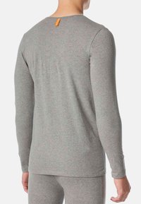 Koszula z długim rękawem w jasnoszarym kolorze, wykonana z miękkiego materiału. Posiada okrągły dekolt oraz pomarańczową metkę z tyłu.