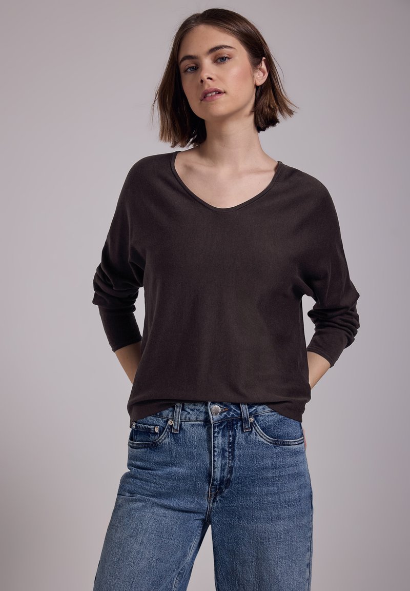 Un haut à manches longues en V marron foncé, fabriqué à partir d'un matériau doux, associé à un jean en denim bleu taille haute avec un lavage vintage.
