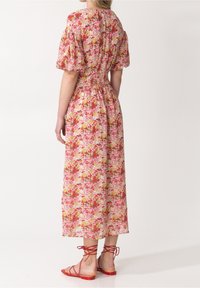 Květinové midi šaty v odstínech růžové, červené a žluté. Mají nafouknuté rukávy, zúžený pas a volný siluetu. Vybavené červenými sandály na podpatku se zavazováním.