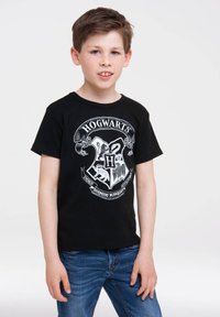 Black cotton T-shirt featuring a white Hogwarts crest graphic. Short sleeves and crew neckline. Paired with blue denim jeans.