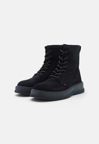 Botas de tobillo de ante negro con punta redonda, con cordones en la parte frontal y una gruesa suela de goma negra. Presentan costuras tonales y una marca mínima.