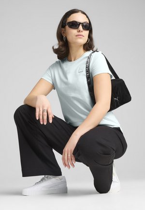 Camiseta de algodón azul claro con mangas cortas y parche de logo, pantalones negros de cintura alta y zapatillas de plataforma blancas. Mochila negra con textura brillante.