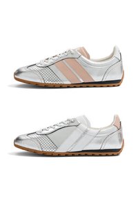 Paire de baskets basses argentées avec semelles en gomme, zones perforées au niveau des orteils, et une chaussure avec des bandes beiges sur le côté.