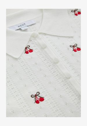 Valge kudumispolo, millel on krae, viis nuppu ning punase ja pruuni kirsi tikand tekstuurse taustaga.