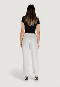 Haut noir à manches courtes côtelé, pantalons de survêtement gris clair avec des poignets élastiques, et baskets à motifs, vus de dos contre un fond neutre.