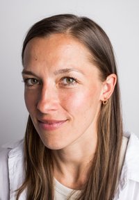 Izbliza portret žene s dugom ravnom smeškom i svetlom kožom, koja nosi zlatnu kružnu naušnicu i belu bluzu.
