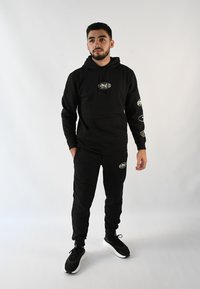Sudadera negra con capucha y joggers a juego hechos de una tela suave; presenta acentos de logo en las mangas; combinado con zapatillas negras.