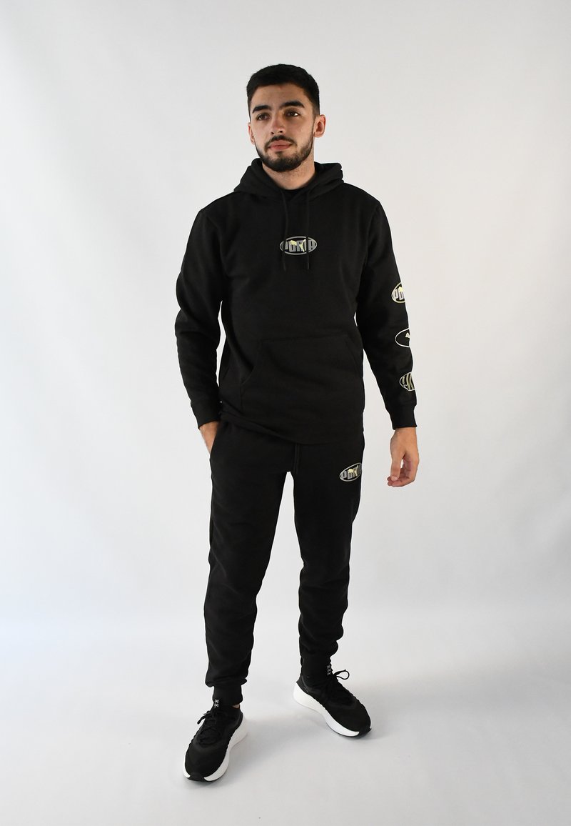 Sudadera negra con capucha y joggers a juego hechos de una tela suave; presenta acentos de logo en las mangas; combinado con zapatillas negras.