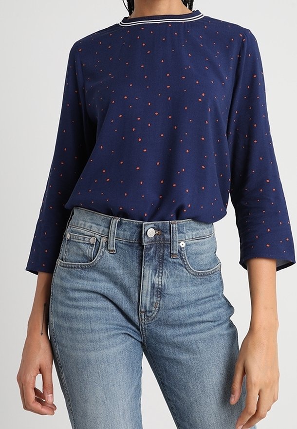 Maglietta a maniche lunghe blu navy con colletto bianco e pois rossi. Abbinata a jeans a vita alta azzurri chiari. Tessuto misto cotone, vestibilità comoda.