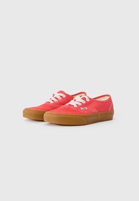 Red canvas sneakers with white laces, rubber gum sole, rounded toe, and stitched accents. Brand logo near the heel.