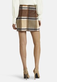 Brūna, bēša un pelēka četru kvadrātu minisekss mīkstā audumā, ar trim vertikālām šuvēm un plakanu jostu. Valkāta ar nude krāsas augstpapēžu kurpēm.