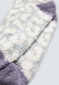 Calcetines suaves en gris claro y blanco con acentos morados, que presentan una superficie texturizada y pequeños puntos antideslizantes claros para mayor agarre.