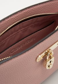 Różowa torebka skórzana o teksturowanym wnętrzu z złotym zamkiem błyskawicznym i elementami metalowymi. Posiada gładkie podszewkę z tkaniny oraz wytłoczone logo marki.