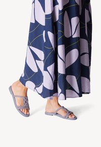 Gray flat sandals with braided straps, paired with a navy dress featuring large light purple and white leaf patterns and yellow accents.