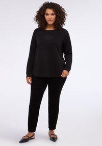 Czarna bluza z wzorem róży na piersi, zestawiona z czarnymi welurowymi spodniami i czarnymi balerinami. Prosty, luźny krój.