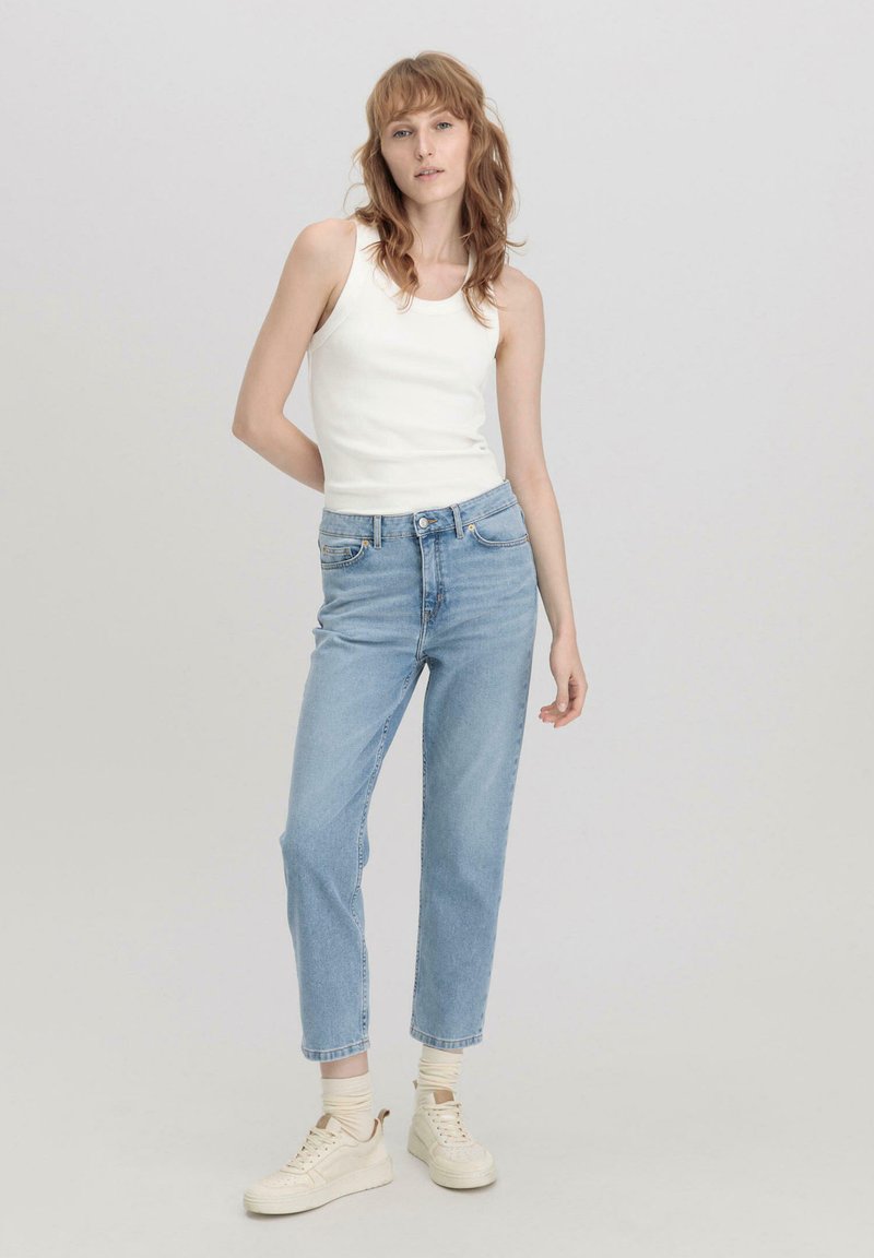 Witte geribde tanktop gecombineerd met hoge lichtblauwe straight-leg jeans en beige sneakers met crèmekleurige sokken.