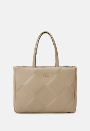 Borsa tote beige trapuntata con doppi manici, con un discreto logo CK. Texture liscia e forma rettangolare con dettagli di cucitura visibili.