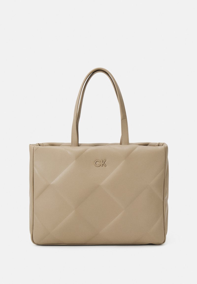 Borsa tote beige trapuntata con doppi manici, con un discreto logo CK. Texture liscia e forma rettangolare con dettagli di cucitura visibili.