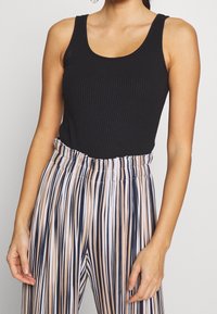 Canotta nera a coste abbinata a pantaloni a righe a vita alta con linee verticali nei toni del blu navy, crema e pesca. Vita elastica.