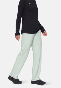 Licht mintgroene broek met een ontspannen pasvorm, gemaakt van lichtgewicht stof, gecombineerd met een zwart langemouwen top en zwarte schoenen.