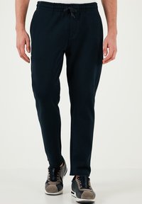Marineblauwe sweatpants van zachte stof met een elastische tailleband en een trekkoord. Gepaard met zwart-grijze sneakers met een suède accent.