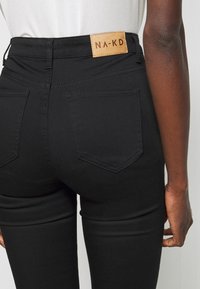 Zwarte high-waisted jeans met een strakke pasvorm, voorzien van een leren label met "NA-KD" aan de achterkant en keurig gestikte zakken.