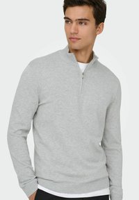 Un sweat à capuche zippé gris clair en tissu doux, avec un col haut, des manches longues et des poignets et un ourlet côtelés pour un look ajusté.