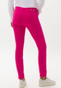 Slim džíny růžové barvy s hladkou texturou, zadními kapsami a vrstvou v pase. V kombinaci s bílými teniskami.