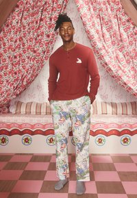 Czerwona koszula henley z długim rękawem i białym logo, zestawiona z wzorzystymi spodniami piżamowymi z kolorowymi ilustracjami, stojąca na szachownicy.