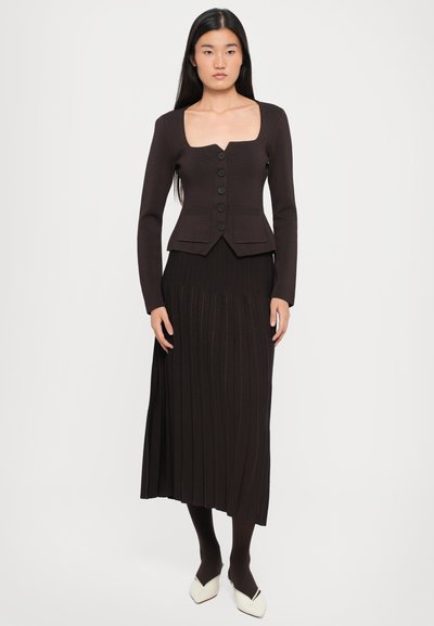 Brown ribbed cardigan with a square neckline and six buttons, paired with a matching pleated skirt. Shoes are white with a pointed toe.