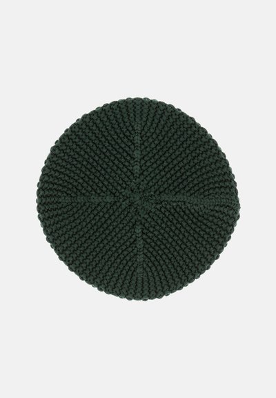 Runder, grüner, gestrickter Teppich mit strukturiertem Oberflächen, der ein Kreuzstichmuster und einen dicken, geflochtenen Rand aufweist.