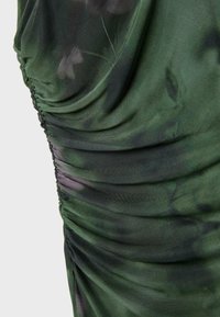 Gros plan sur un tissu froncé de couleur vert foncé et noir avec un motif subtil tie-dye et des coutures visibles le long de la couture latérale froncée.