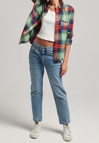 Camicia a quadri colorata in verde, rosso e blu, indossata sopra una canotta bianca; jeans blu a vita alta e sneaker bianche.