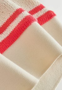 Tissu en maille côtelée rayé crème et rouge plié, montrant les détails de la texture et du motif sur un matériau textile doux.