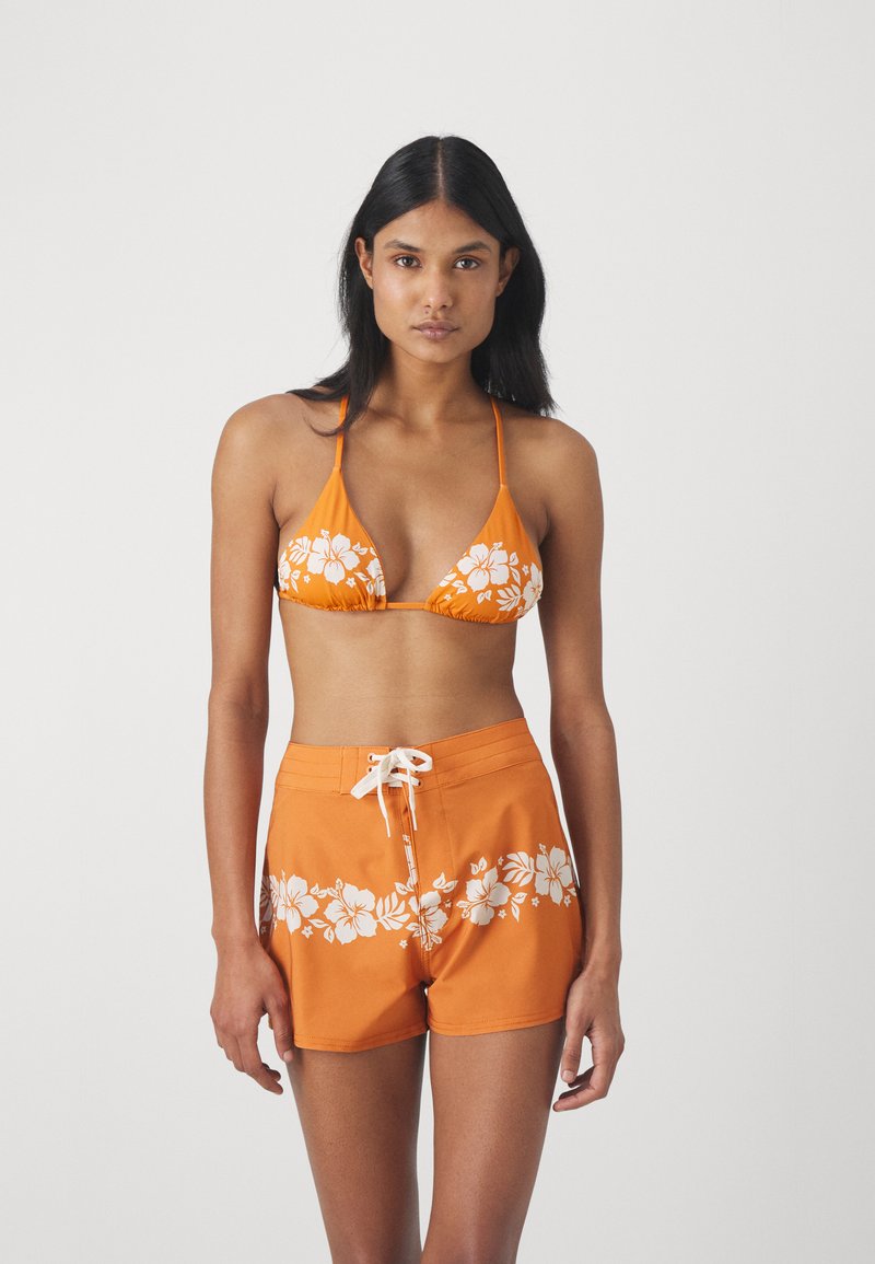 Haut de bikini orange avec un motif floral blanc, associé à un short de bain orange portant le même design. Bretelles réglables et lien à l'avant.