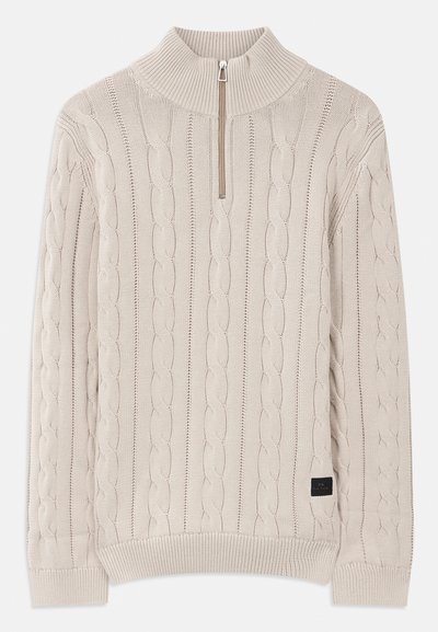 Šviesiai rudas megztinis su pleištų raštu, ilgomis rankovėmis, dygsniuotomis rankogaliais ir apykaite su ketvirčio užtrauktuku.