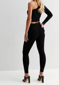 Jeans skinny neri a vita alta abbinati a un top nero a spalla unica. Presentano una texture liscia e un design aderente.