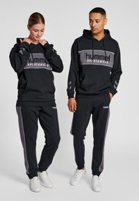 Svart hoodie och joggers-set med grå accenter. Har logga på framsidan, kenguruficka och kontrasterande sidsränder. Material av bomullsblandning.