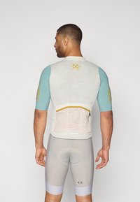 Maillot de cyclisme pour hommes en crème clair avec des manches courtes turquoise, doté d'un tissu texturé et d'une poche zippée à l'arrière. Cuissard de cyclisme gris avec rembourrage.