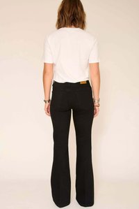 Jean noir évasé avec une coupe classique, doté de poches arrière et d'une étiquette de marque en cuir tan au-dessus de la poche droite, associé à un t-shirt blanc.