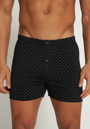Zwarte boxershort met een wit stippenpatroon, elastische tailleband, knoopgulp en een logo-label op de taille. Een zachte stoftextuur.