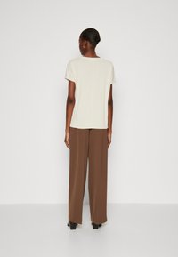 Top a maniche corte color beige chiaro con taglio dritto, abbinato a pantaloni larghi marroni e scarpe con tacco a blocco nere; silhouette semplice e pulita.