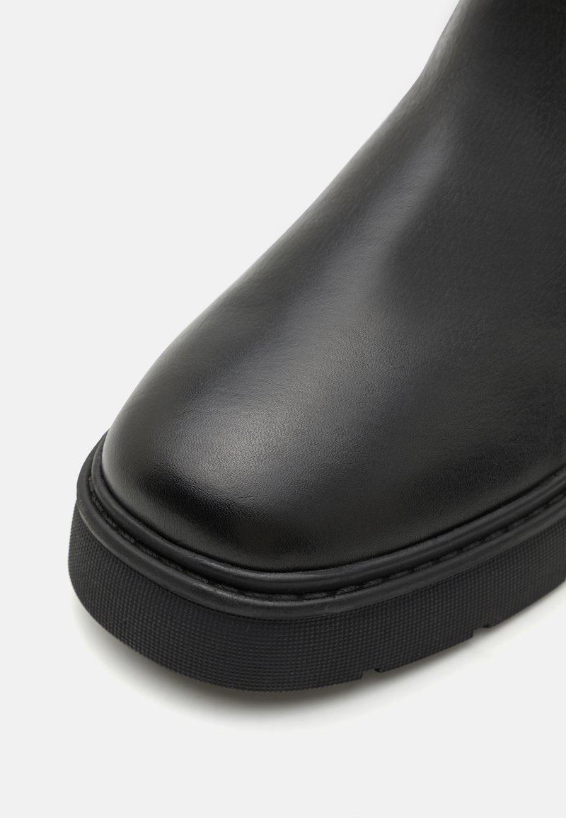 Schwarzer Lederstiefel mit runder Zehenform, strukturiertem schwarzen Gummisohle und genähten Details entlang der Kante. Glatte Oberfläche, minimalistisches Design.