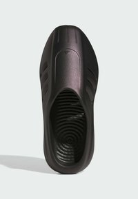 En ensam svart slip-on sko med texturerad innersula och tre sidostripes, sedd ovanifrån på en ljusgrå bakgrund.
