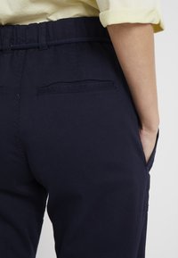 Mörkblå byxor med reglerbart midjeband, sidofickor och två bakfickor, tillverkade av ett mjukt och slitstarkt material.