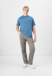 Blå bomull crew-neck t-skjorte med korte ermer og en liten trykt etikett på fronten, sammen med lysegrå, teksturerte bukser og hvite joggesko.