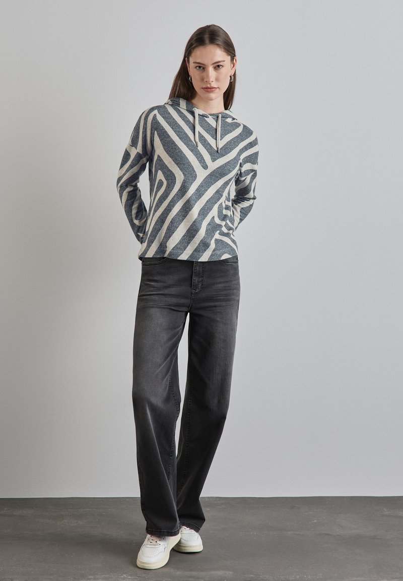 Grå och krämrandig hoodie med dragsko, kombinerad med lösa mörka jeans och vita sneakers. Enkelt design med en avslappnad passform.